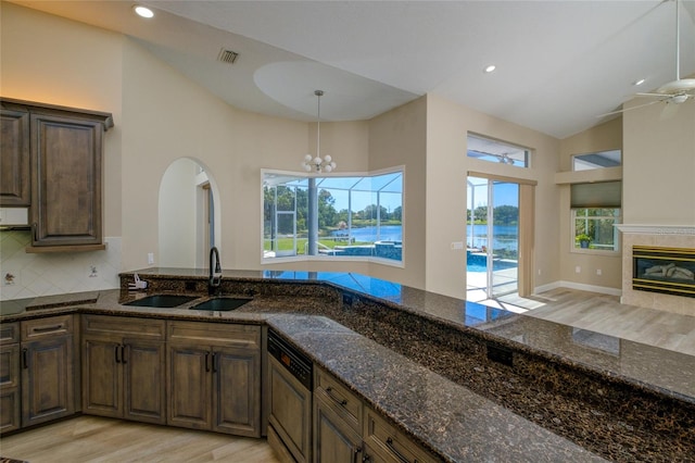 kitchen with light wood-type flooring, ceiling fan with notable chandelier, sink, and dark stone countertops