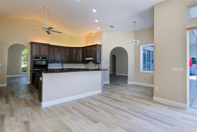 kitchen with ceiling fan with notable chandelier, range hood, high vaulted ceiling, light hardwood / wood-style floors, and pendant lighting