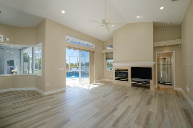 unfurnished living room with ceiling fan, a wealth of natural light, light wood-type flooring, and high vaulted ceiling