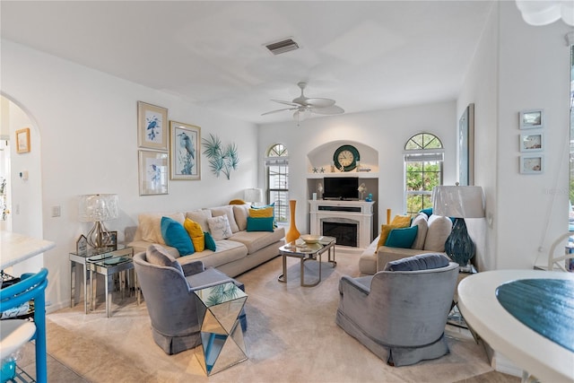 living room featuring ceiling fan, a fireplace, visible vents, and arched walkways