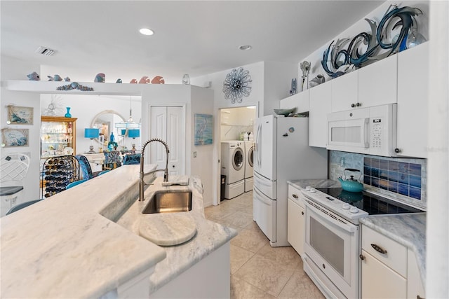 kitchen with white appliances, tasteful backsplash, white cabinets, washer and dryer, and a sink