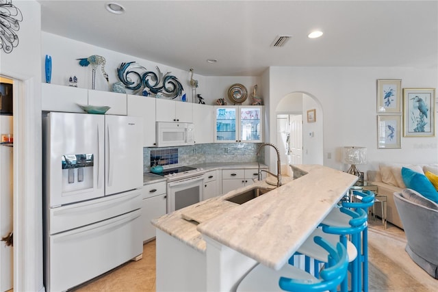 kitchen with white appliances, visible vents, arched walkways, a kitchen bar, and a sink