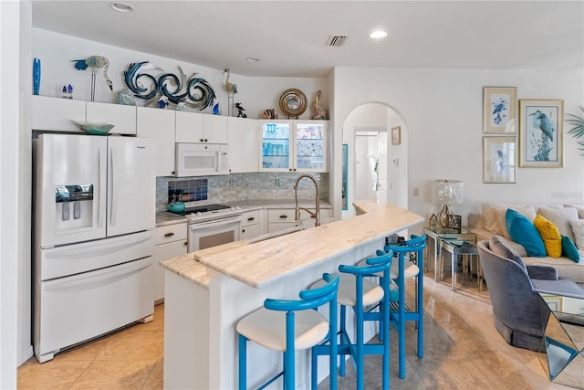 kitchen with white appliances, arched walkways, white cabinets, a kitchen breakfast bar, and open floor plan