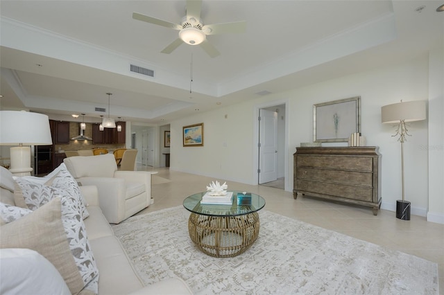 tiled living room featuring ornamental molding, a raised ceiling, and ceiling fan