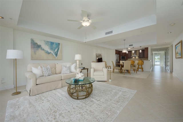 living room with a tray ceiling, ornamental molding, ceiling fan, and light tile patterned flooring