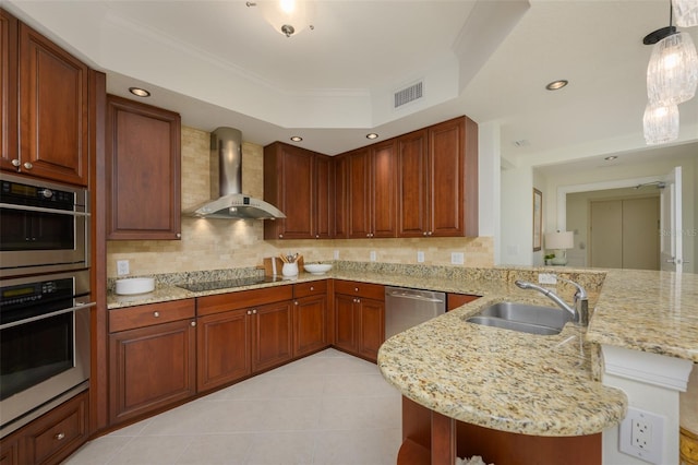 kitchen featuring sink, appliances with stainless steel finishes, hanging light fixtures, kitchen peninsula, and wall chimney exhaust hood