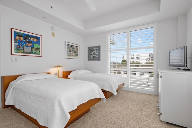 bedroom with a raised ceiling, light colored carpet, and ceiling fan