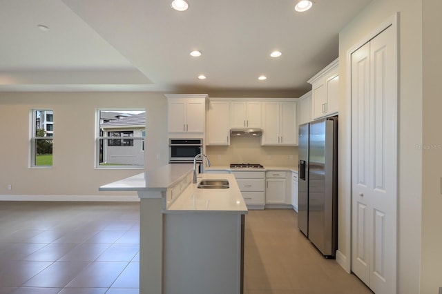 kitchen featuring sink, light tile floors, a center island with sink, stainless steel appliances, and white cabinetry