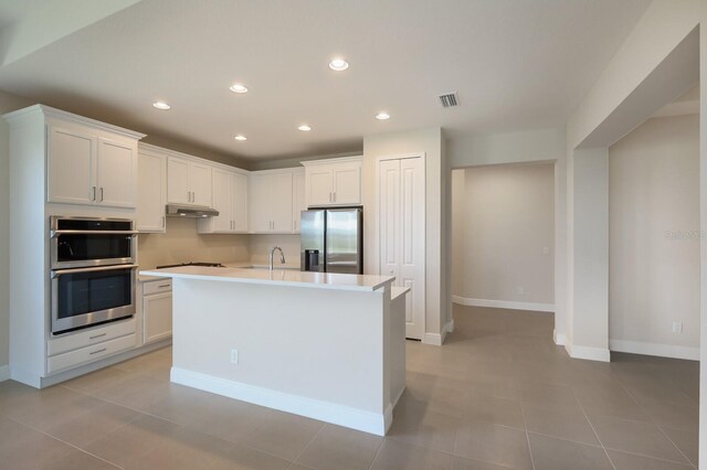 kitchen with an island with sink, light tile floors, appliances with stainless steel finishes, white cabinets, and sink