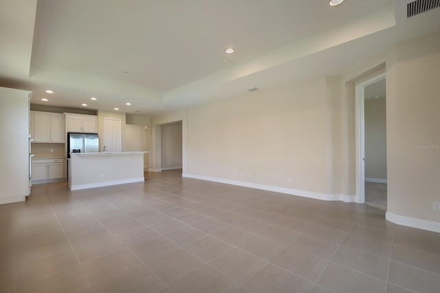 unfurnished living room featuring a raised ceiling and light tile floors