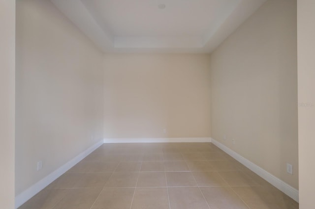 empty room with light tile flooring and a tray ceiling