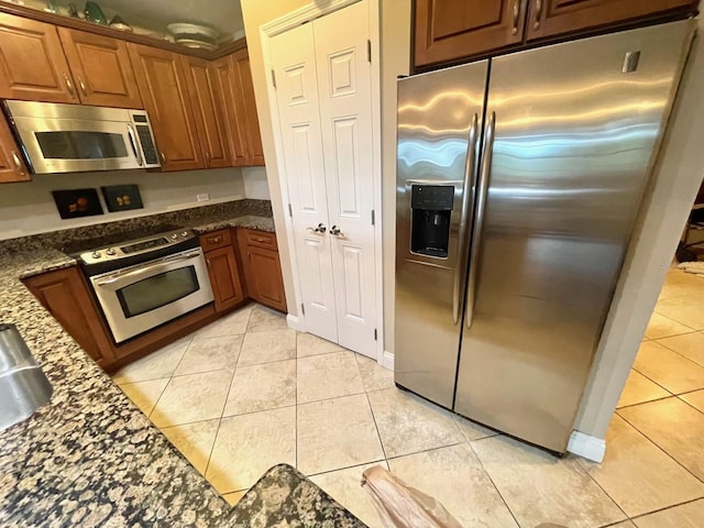 kitchen with light tile floors, dark stone counters, and stainless steel appliances