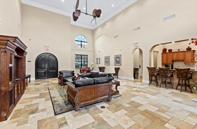 living room featuring a high ceiling, a chandelier, light tile floors, and ornamental molding