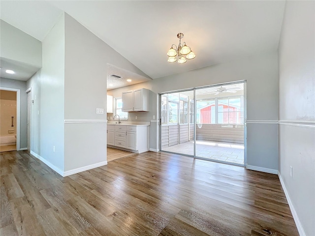 empty room featuring sink, light hardwood / wood-style floors, ceiling fan with notable chandelier, and vaulted ceiling