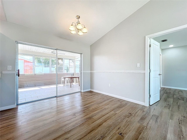 unfurnished room with an inviting chandelier, vaulted ceiling, and light hardwood / wood-style flooring