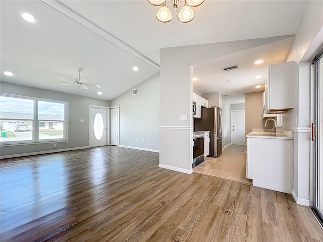 unfurnished living room with lofted ceiling, ceiling fan with notable chandelier, sink, and light wood-type flooring