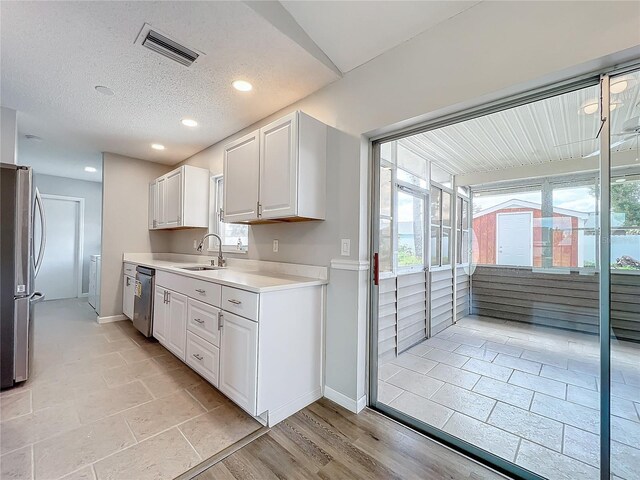 kitchen with stainless steel appliances, a textured ceiling, white cabinetry, light wood-type flooring, and sink