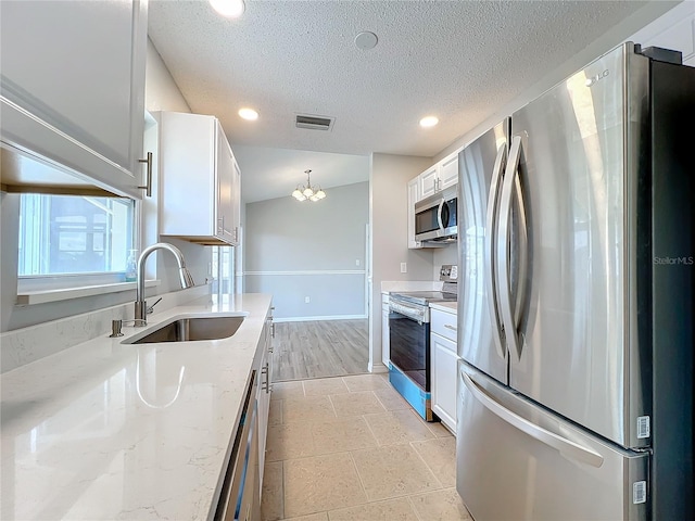 kitchen with appliances with stainless steel finishes, white cabinets, a notable chandelier, light stone countertops, and sink