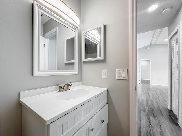 bathroom with lofted ceiling, hardwood / wood-style floors, vanity, and a textured ceiling