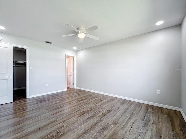 unfurnished bedroom with a walk in closet, a closet, ceiling fan, and wood-type flooring