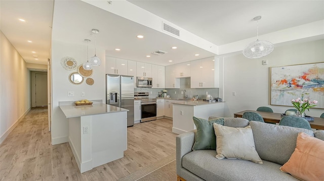 kitchen featuring stainless steel appliances, hanging light fixtures, open floor plan, white cabinetry, and a peninsula