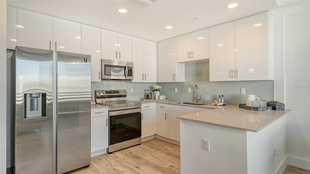 kitchen featuring stainless steel appliances, light countertops, white cabinets, a sink, and a peninsula