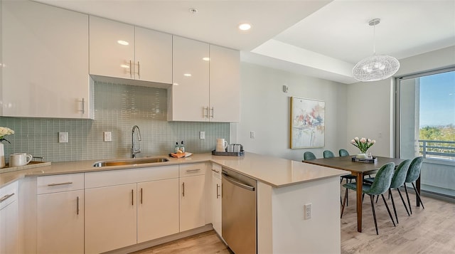 kitchen featuring light countertops, decorative light fixtures, a peninsula, and stainless steel dishwasher