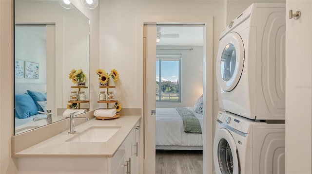 laundry room with laundry area, light wood finished floors, a sink, and stacked washer / drying machine