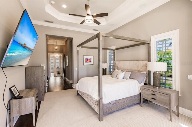 bedroom featuring a tray ceiling, hardwood / wood-style floors, ceiling fan with notable chandelier, and ornamental molding