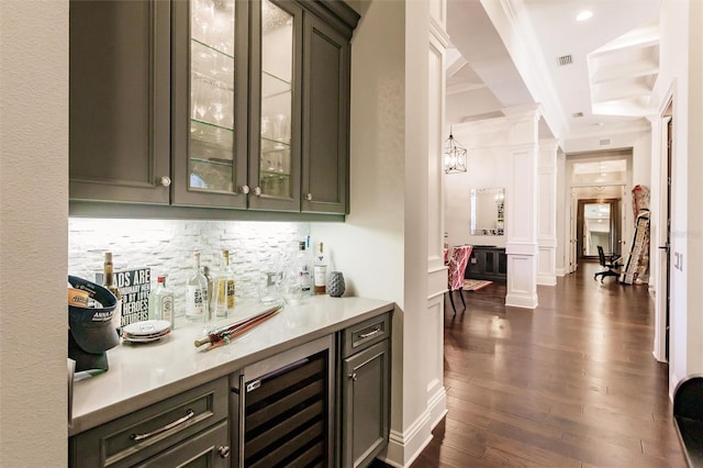 bar with dark wood-type flooring, crown molding, ornate columns, tasteful backsplash, and beverage cooler