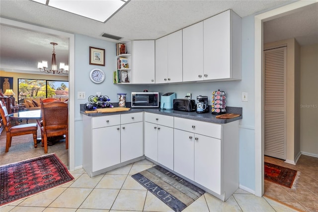 kitchen with light tile patterned floors, visible vents, dark countertops, a textured ceiling, and a notable chandelier