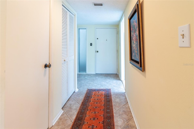 hallway featuring light tile patterned floors, baseboards, and visible vents