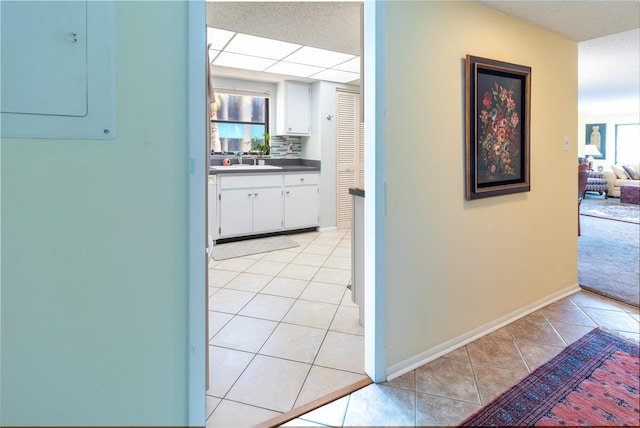 hall with light tile patterned flooring, a sink, electric panel, and baseboards