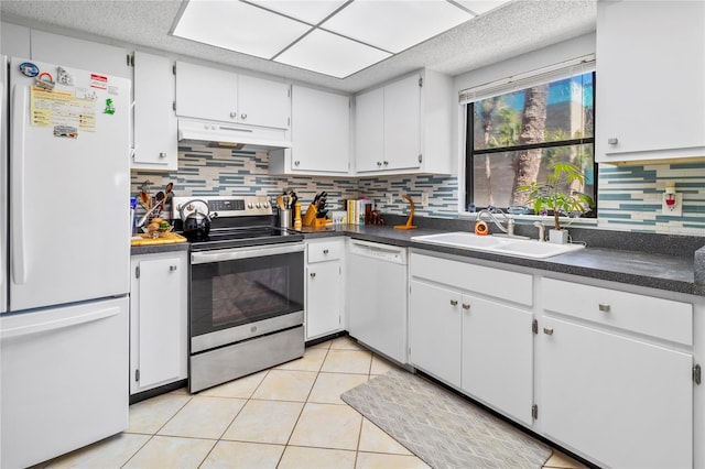 kitchen featuring white appliances, light tile patterned floors, dark countertops, under cabinet range hood, and a sink