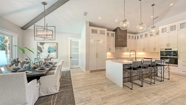 kitchen featuring a center island with sink, lofted ceiling with beams, decorative light fixtures, and double oven