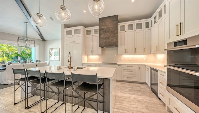 kitchen with white cabinetry, a kitchen breakfast bar, decorative light fixtures, a kitchen island with sink, and custom range hood