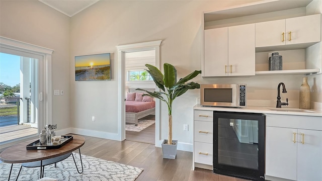 interior space with wine cooler, white cabinetry, sink, and hardwood / wood-style flooring