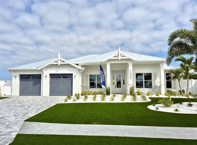 modern inspired farmhouse with an attached garage, metal roof, a porch, and decorative driveway