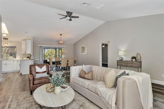 living room featuring vaulted ceiling, light hardwood / wood-style floors, and ceiling fan with notable chandelier