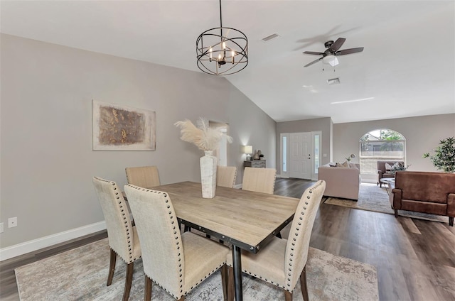 dining room featuring ceiling fan with notable chandelier, vaulted ceiling, and dark wood-type flooring