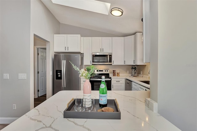 kitchen featuring dark hardwood / wood-style floors, vaulted ceiling with skylight, white cabinets, stainless steel appliances, and light stone countertops