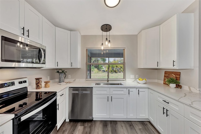 kitchen featuring sink, white cabinets, stainless steel appliances, decorative light fixtures, and light wood-type flooring