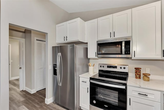 kitchen featuring lofted ceiling, white cabinetry, light hardwood / wood-style flooring, stainless steel appliances, and light stone counters