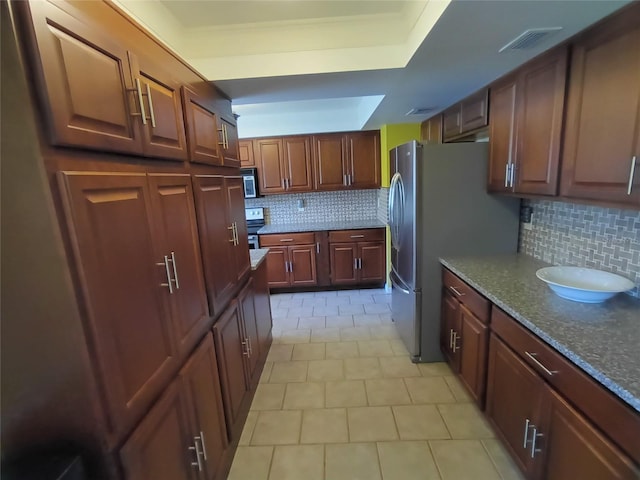 kitchen featuring decorative backsplash, stainless steel appliances, a tray ceiling, and dark stone countertops