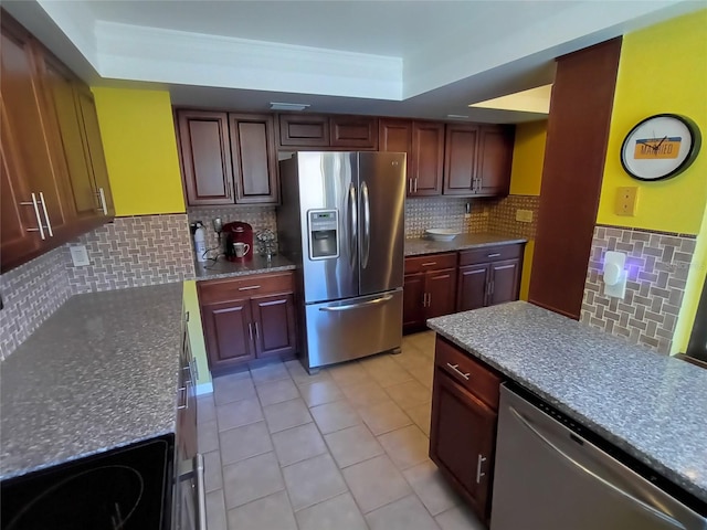 kitchen with tasteful backsplash, a tray ceiling, light tile patterned flooring, and appliances with stainless steel finishes