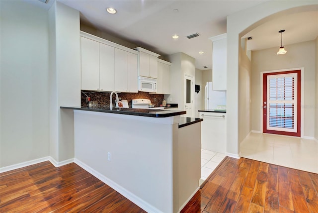 kitchen featuring kitchen peninsula, tasteful backsplash, white appliances, white cabinets, and light wood-type flooring