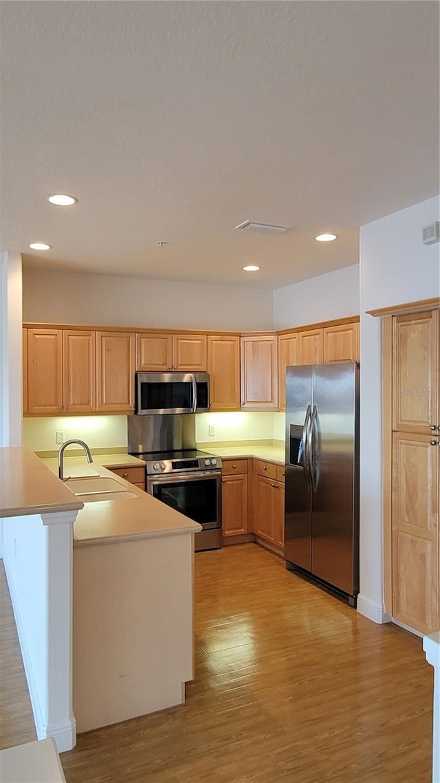 kitchen with light brown cabinets, kitchen peninsula, stainless steel appliances, sink, and light wood-type flooring