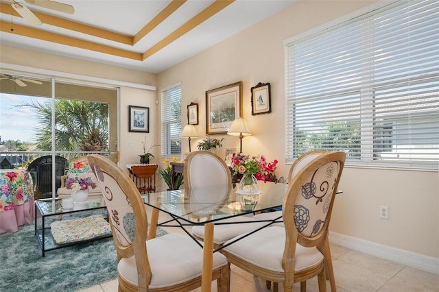 tiled dining space with a raised ceiling and ceiling fan