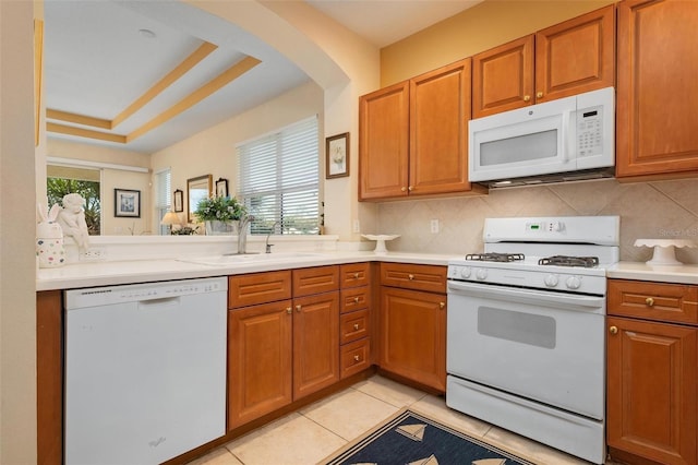 kitchen with backsplash, a tray ceiling, white appliances, sink, and light tile floors