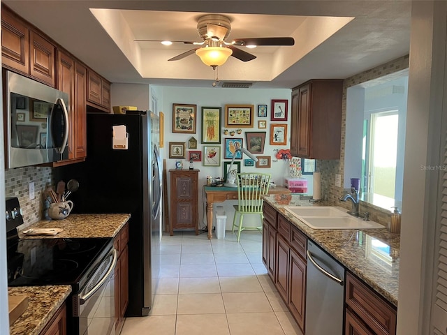 kitchen featuring a tray ceiling, tasteful backsplash, stainless steel appliances, light tile floors, and sink